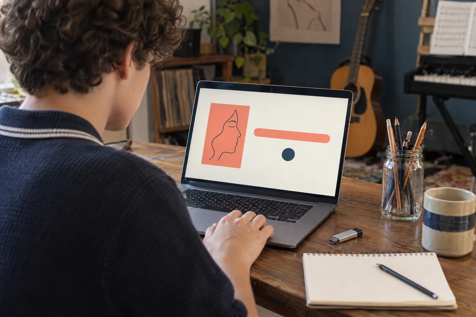 A teenager with curly hair in a navy knit polo at a music room looks at a screen showing a software product for sale, with a glass jar of pencils beside them.