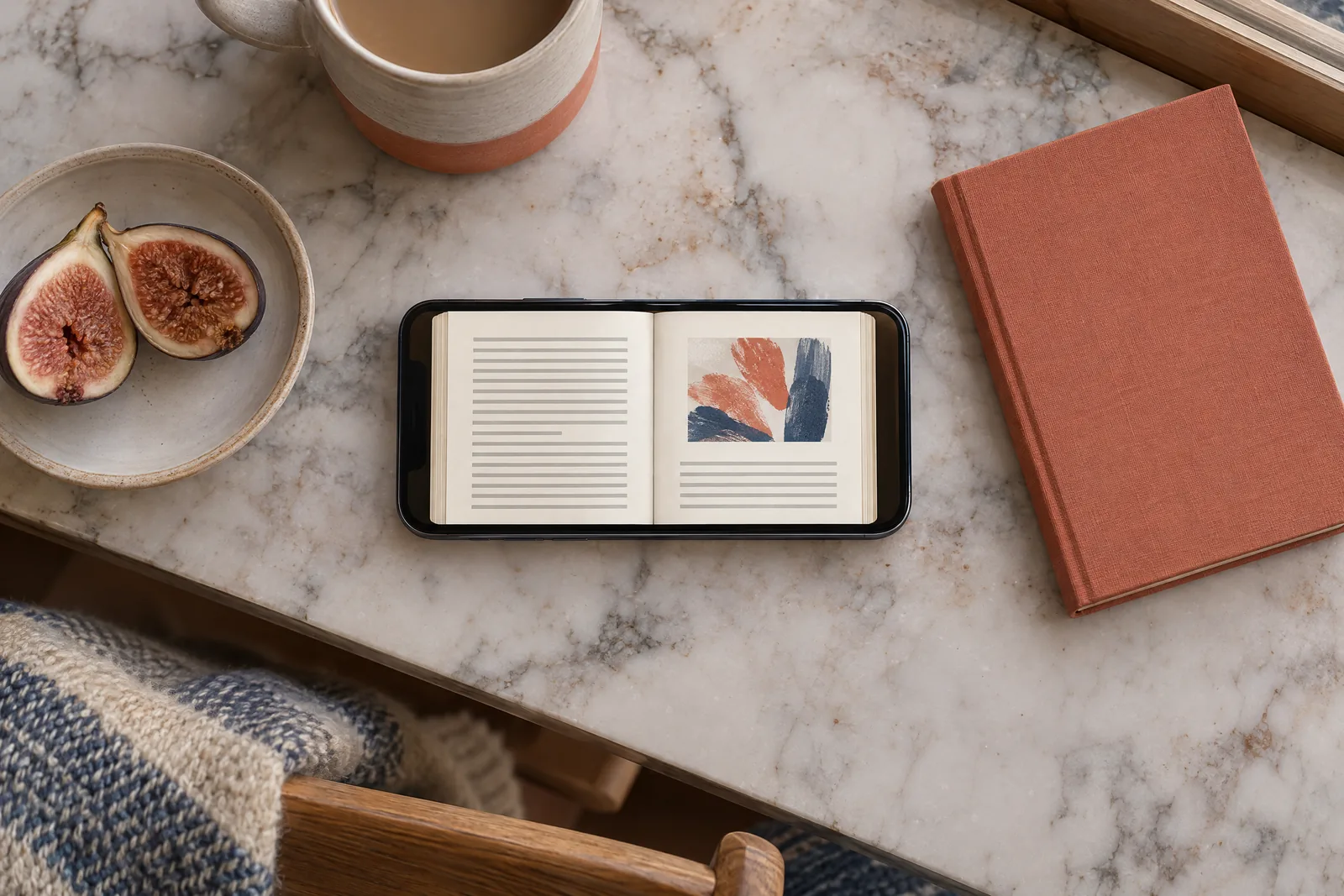 A cabin desk still life of a book product arranged with a split fig, in coral, sand, slate, and cream.