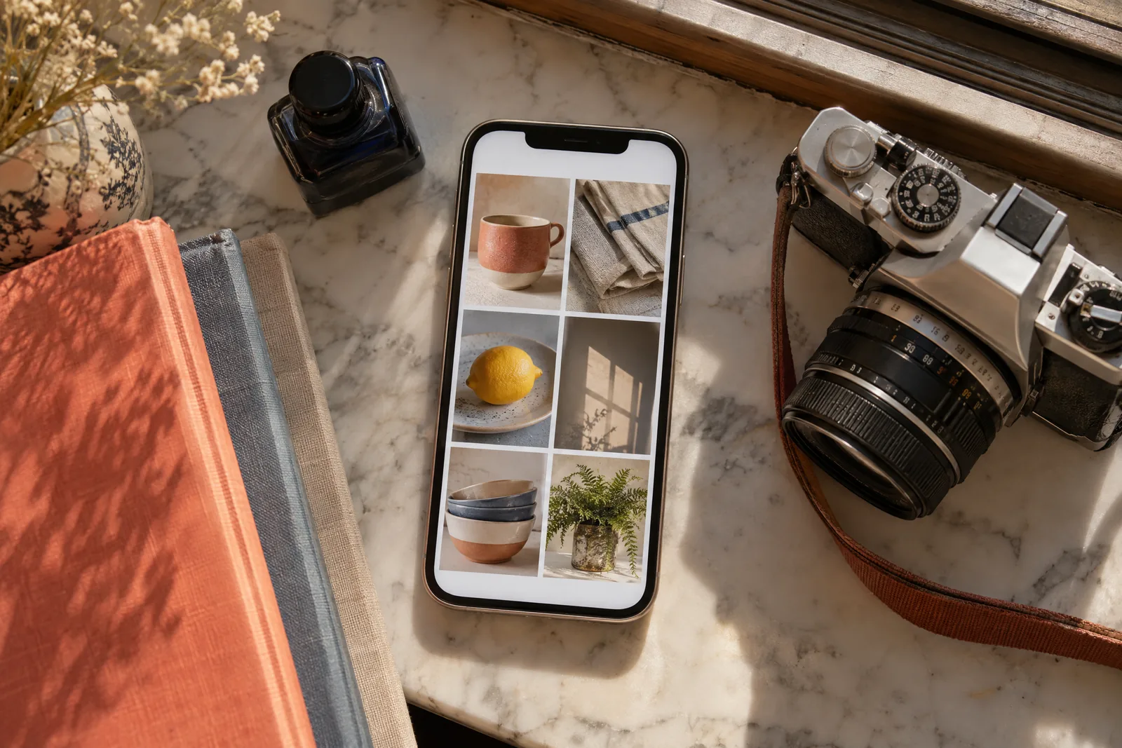 A library carrel still life of a photo product arranged with a small ink bottle, in coral, sand, slate, and cream.