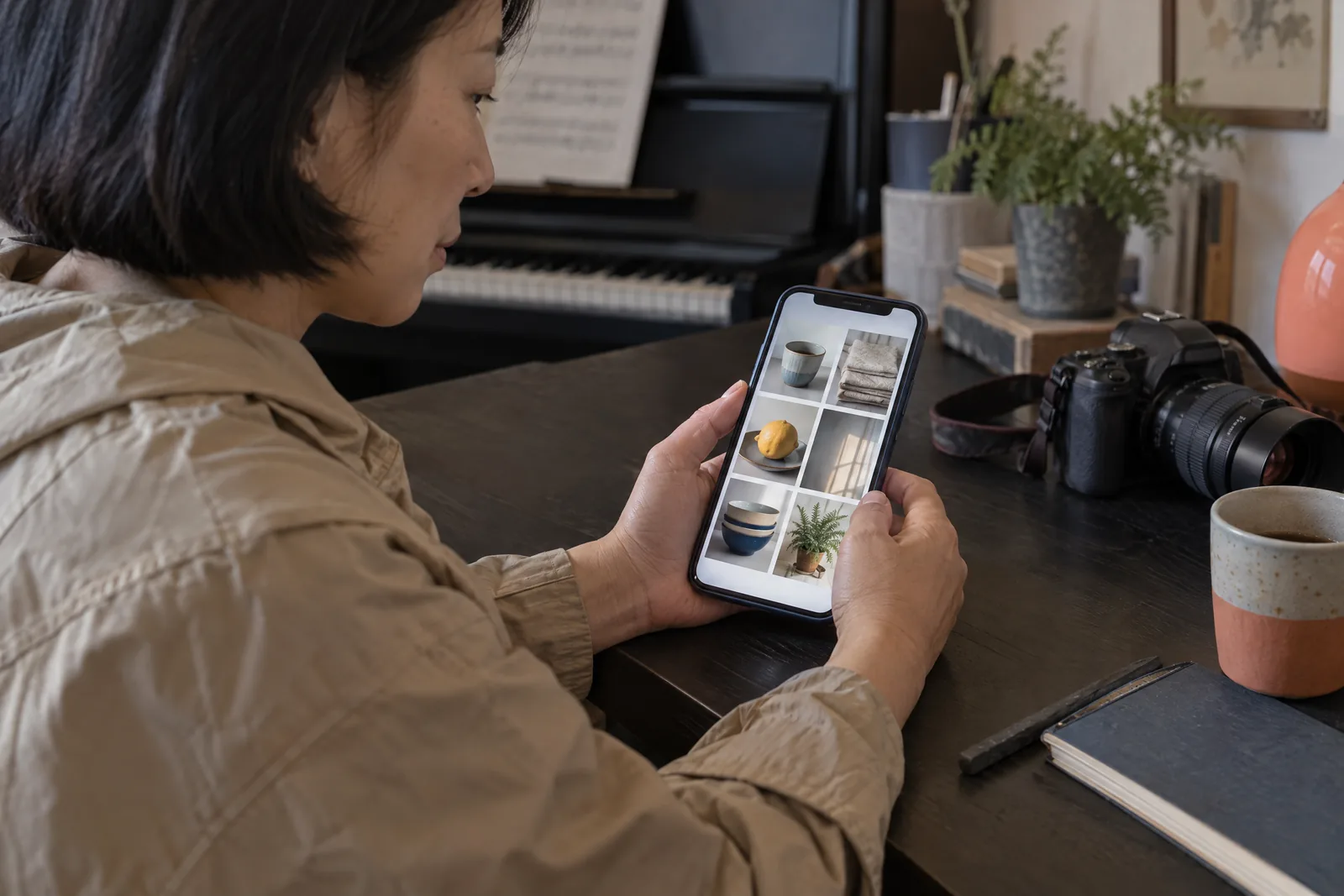 An east asian woman in her forties with a short bob in a sand rain jacket at a music room looks at a screen showing a photo product for sale, with a charcoal stick beside them.