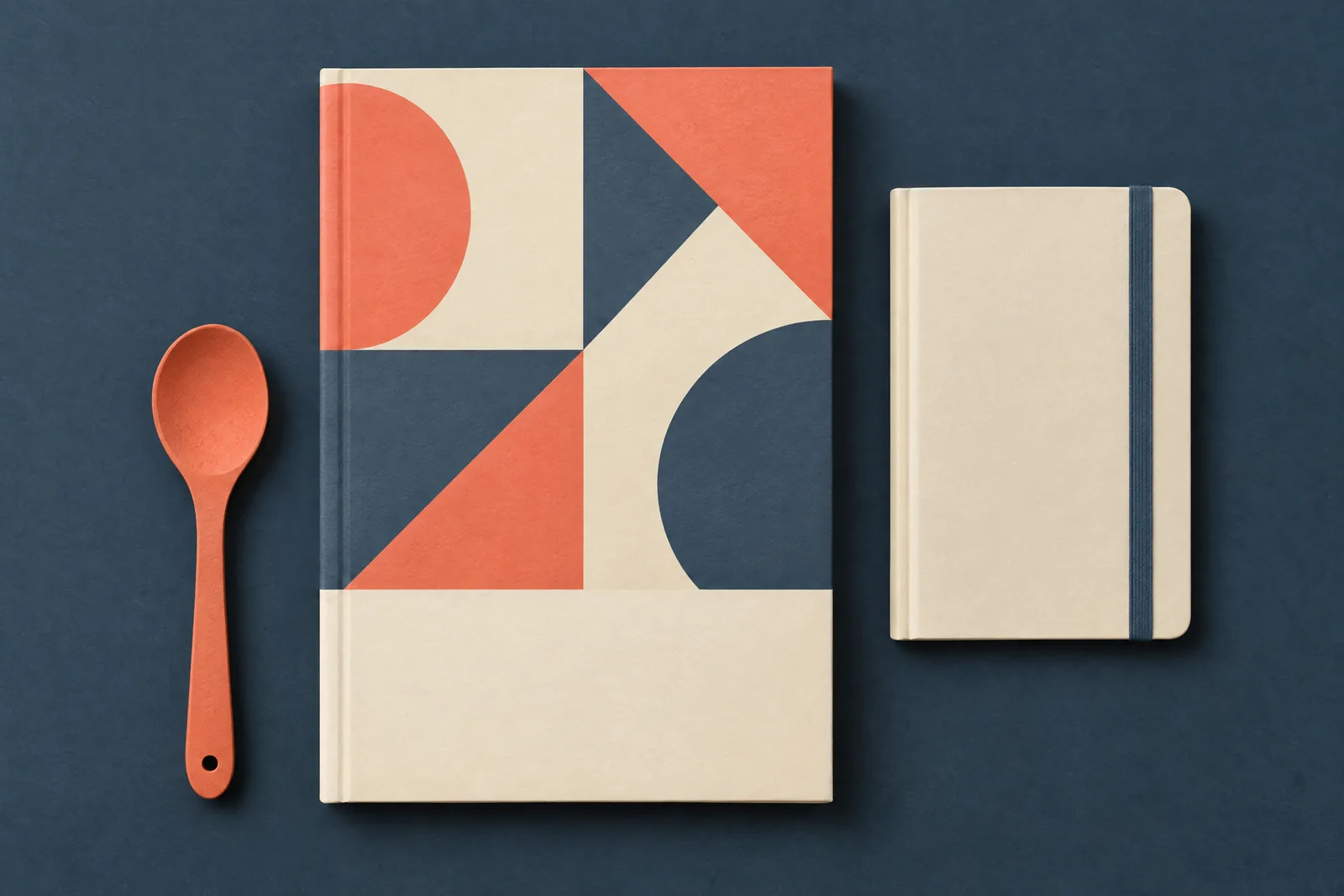 A basement studio still life of a ebook product arranged with a wooden spoon, in coral, sand, slate, and cream.