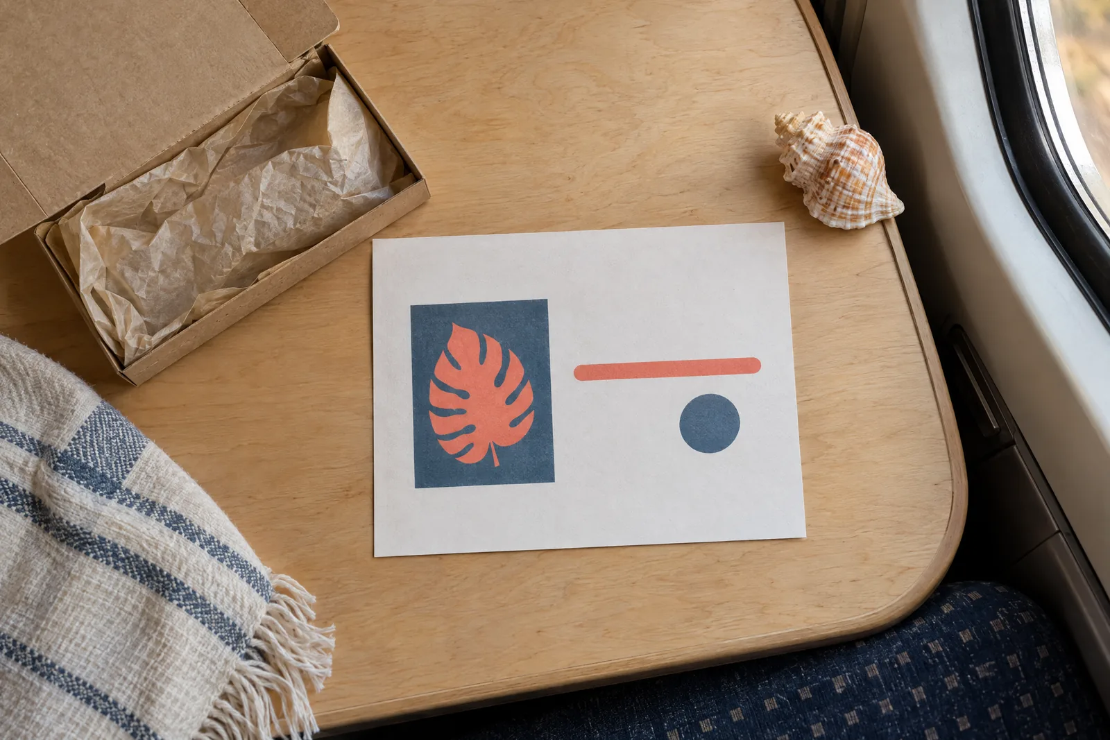 A train compartment still life of a delivery product arranged with a seashell, in coral, sand, slate, and cream.