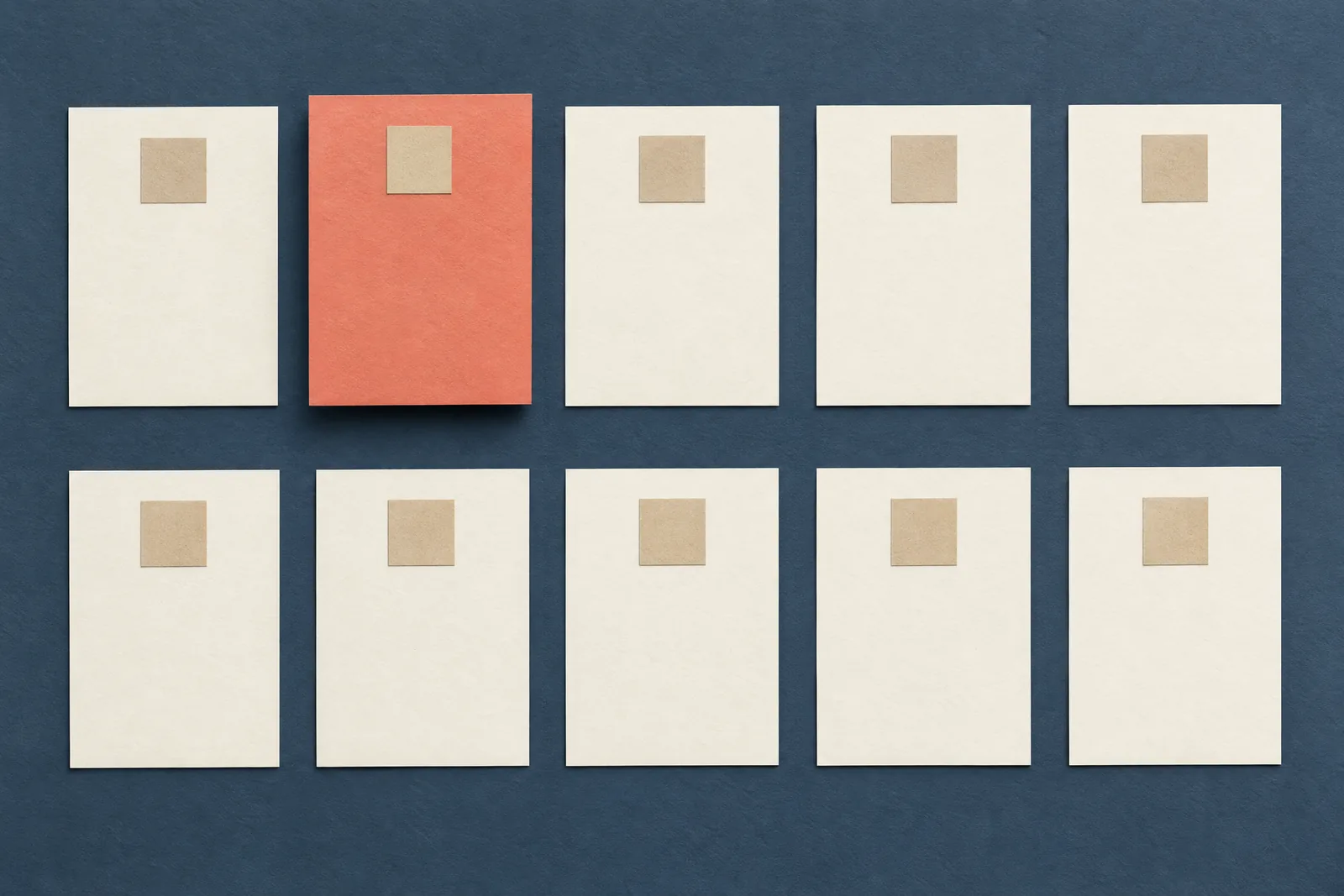 Paper collage of ten catalog cards in two rows of five on slate, with one coral card raised above the rest.